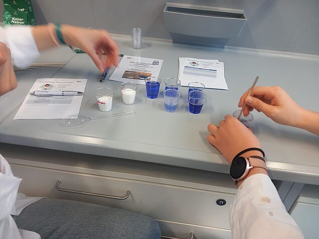 Das Experiment "Wie wird blaue Tinte unsichtbar?"
Man sieht mehrere kleine Becher mit unterschiedlich intensiv blauen Flüssigkeiten, eine blubbert sichtbar.